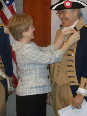 Diana Ritter, Regent, Independence Pioneers DAR Chapter, also participated in the ceremony by placing the SAR Rosette on Compatriot Quint's lapel.